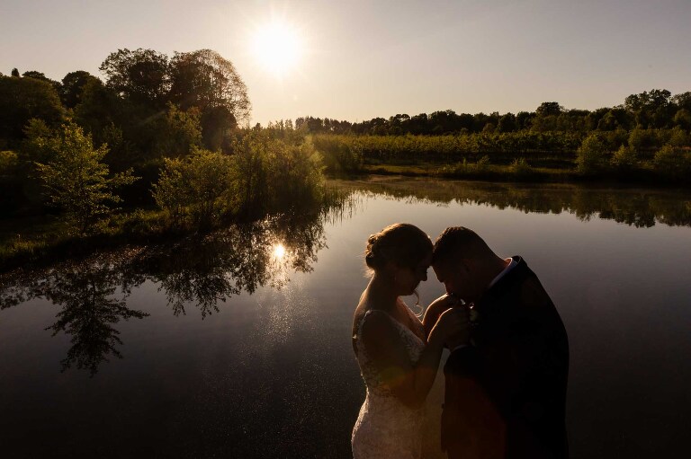 sunset silhouette of a bride and groom snuggling together, surrounded by water, at sunset at the pinehall at eisler farms wedding venue
