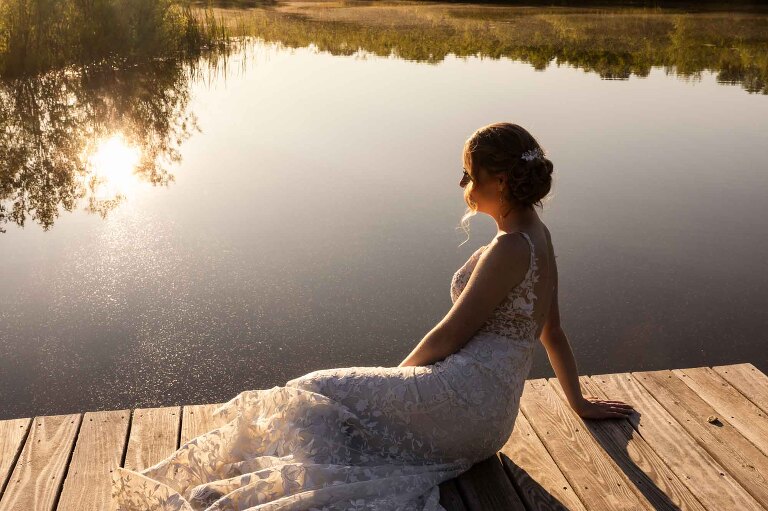 timeless portrait of bride sitting on a dock in front of lake water at the butler wedding venue pinehall at eisler farms