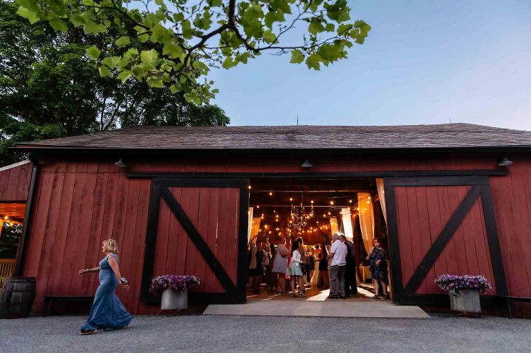 sunset picture of wedding venue with people dancing in the barn and people walking outside, taken at the barn venue outside butler, pinehall at eisler farms