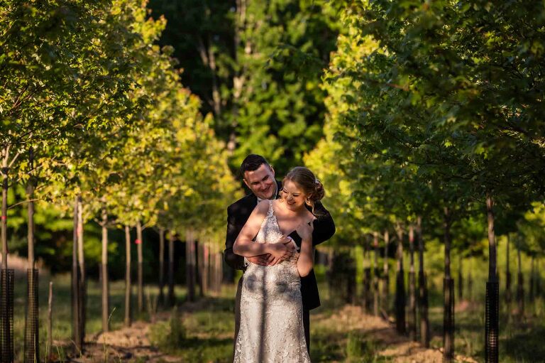 bride and groom posing in between rows of trees growing on the eisler farm wedding venue, pinehall