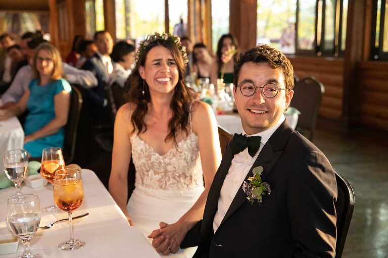 bride and groom sit together at dinner table holding hands, a detail that a photojournalist who photographs weddings is always looking for