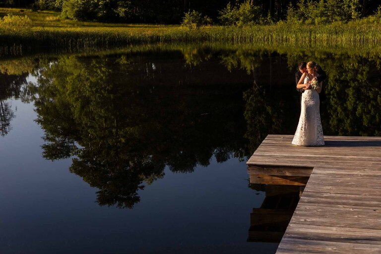 bride and groom snuggle together on a dock over a lake at pinehall at eisler farms wedding venue