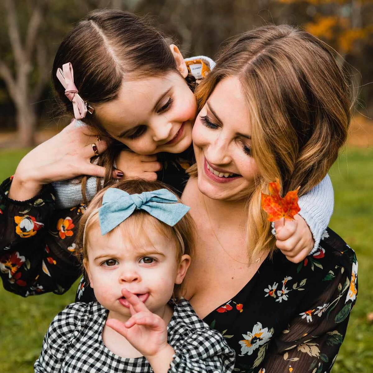 candid picture of mom and her two little girls snuggling together while the youngest stares pensively at the camera