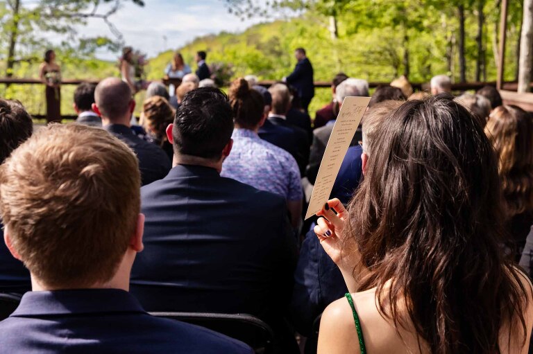 wedding guests shield their face with wedding programs from the sun, during the patio wedding ceremony at Adventures on the Gorge