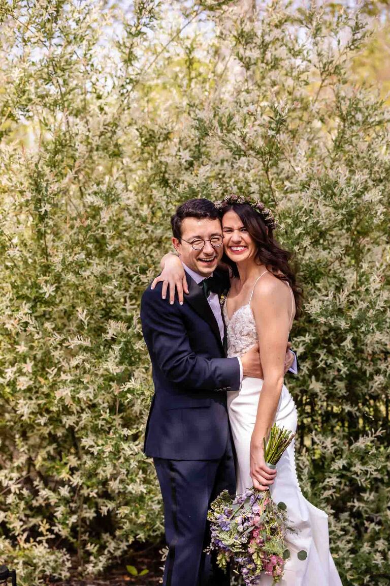 fun relaxed portrait of bride and groom in front of spring flowers, with their faces squished together. relaxed candid feeling portraits are the goal of any photojournalist who photographs weddings