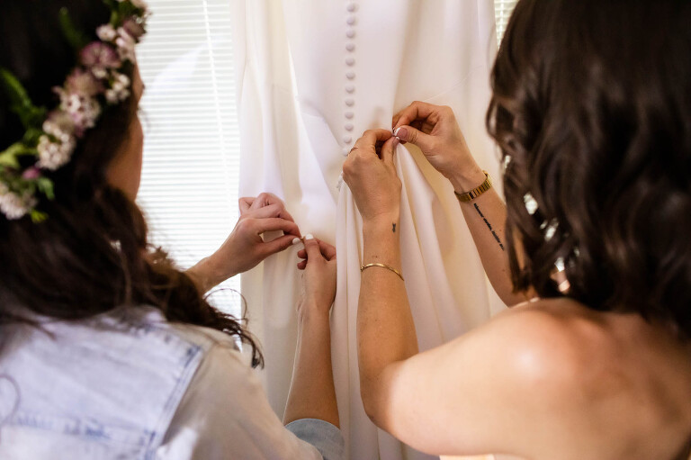 close up picture of bride and her bridesmaid working together to prepare the wedding dress