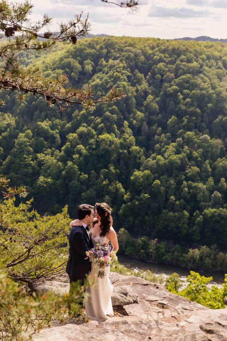 bride and groom stand on a cliff overlooking the west virginia gorge, at their adventures on the gorge wedding