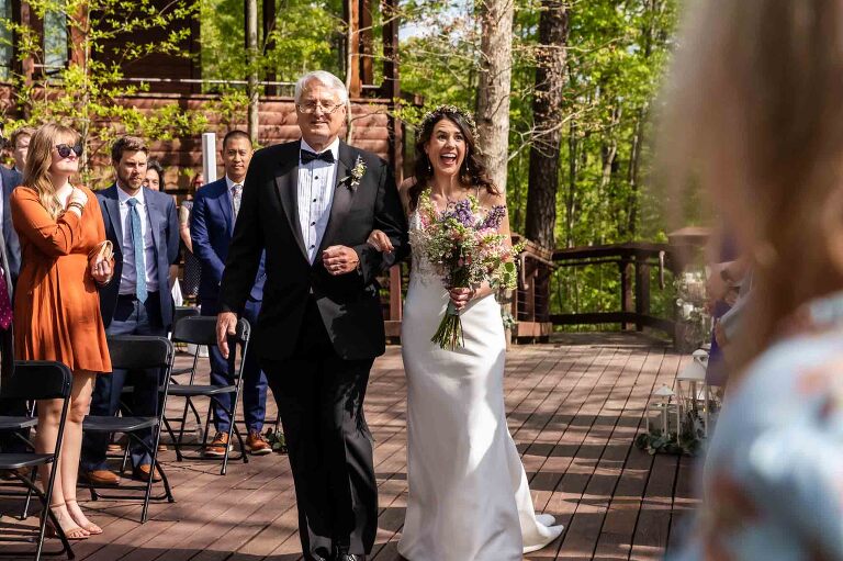 bride laughs as she walks up the aisle with her dad, surrounded by family and friends, overlooking the beautiful scenic west virginia gorge