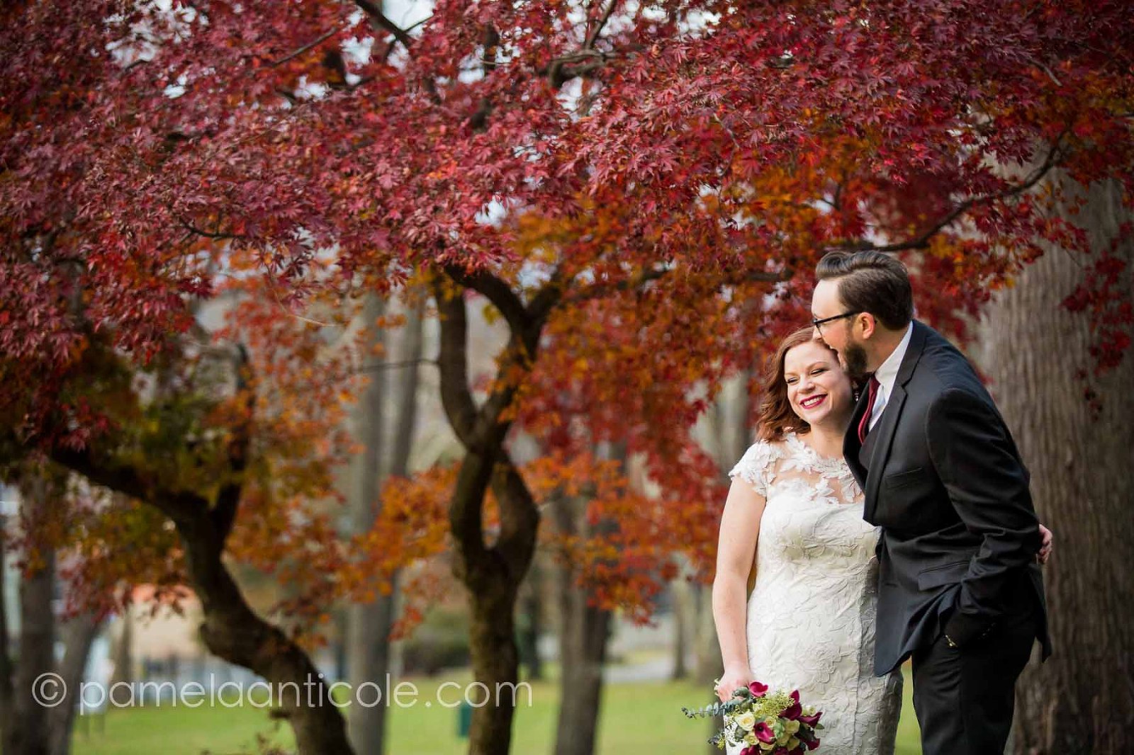 bride and groom laugh together in allegheny cemetery, in front of a red tree in the autumn