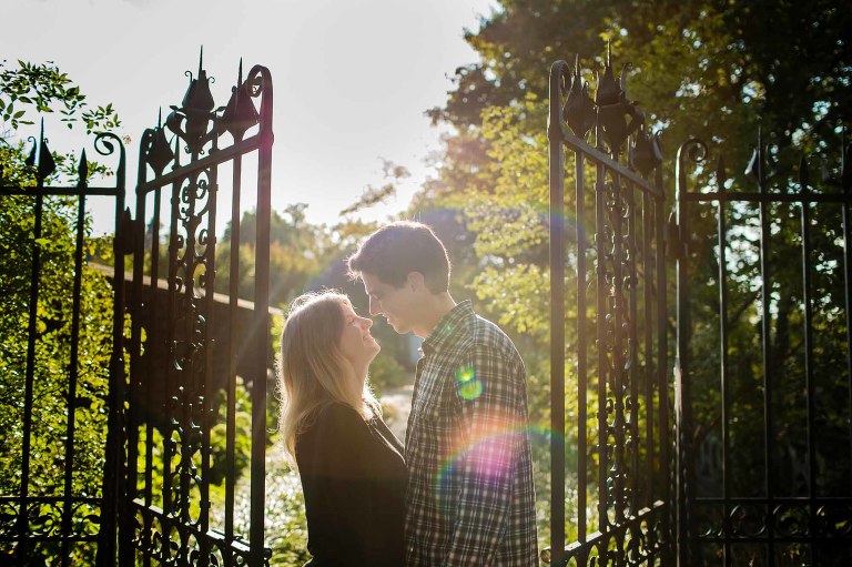 bride and groom gazing into each others' eyes, framed by an ornate iron gate, with sunset sun flare, on their engagement session at mellon park in pittsburgh