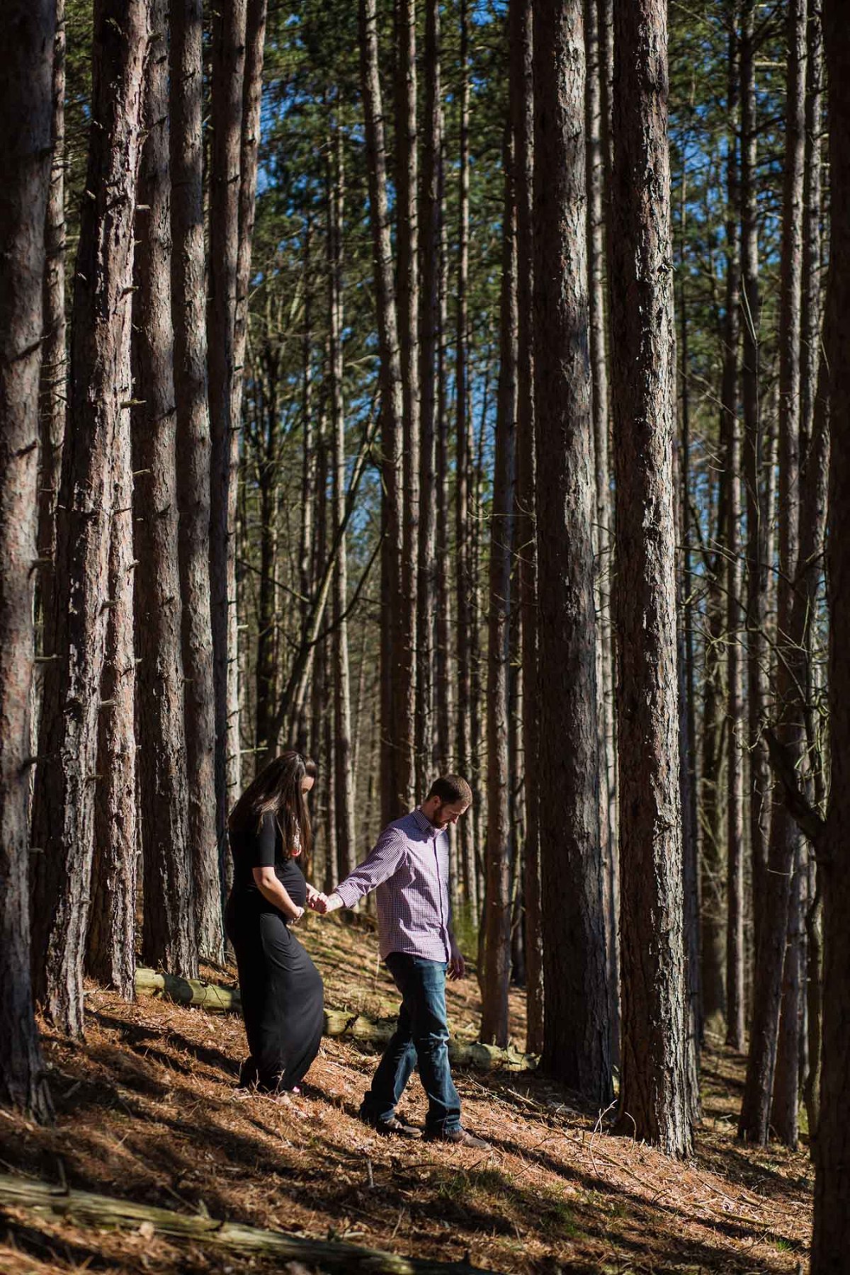 husband leading pregnant wife down through tall trees in the woods