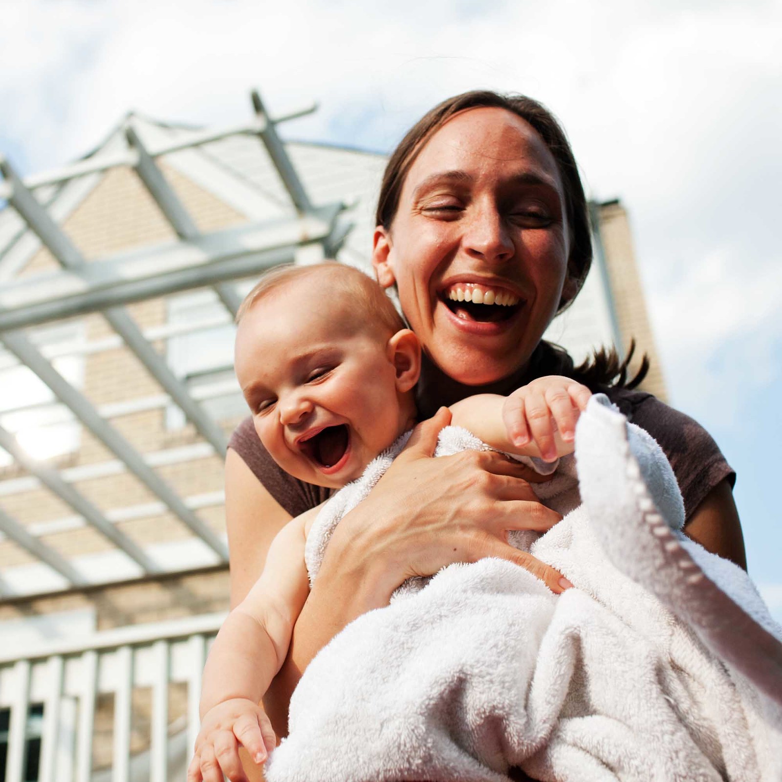 woman laughs with baby, holding in her arms, with white fluffy blanket