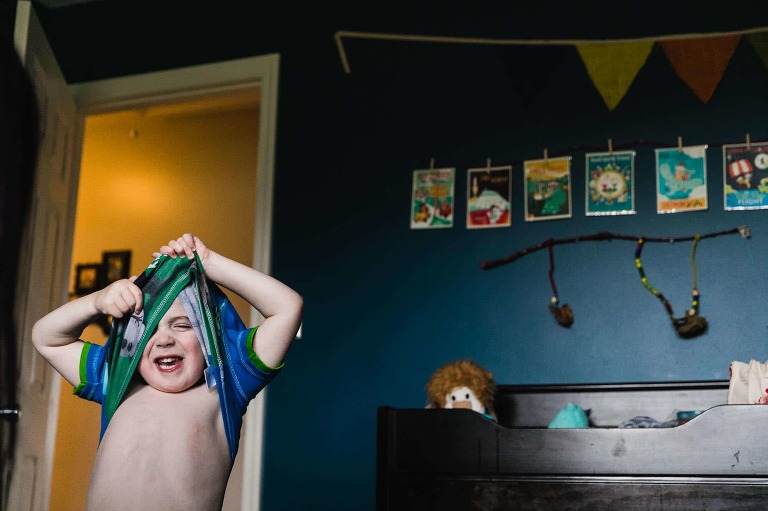little boy struggling to get dressed, pulling his pajamas over his head and getting stuck