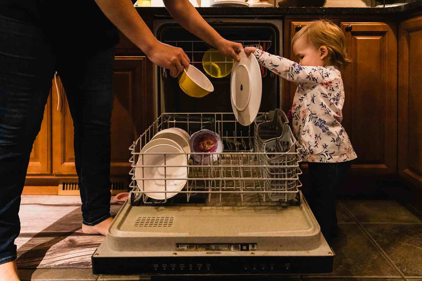 little girl helps mom take dishes out of the dishwasher