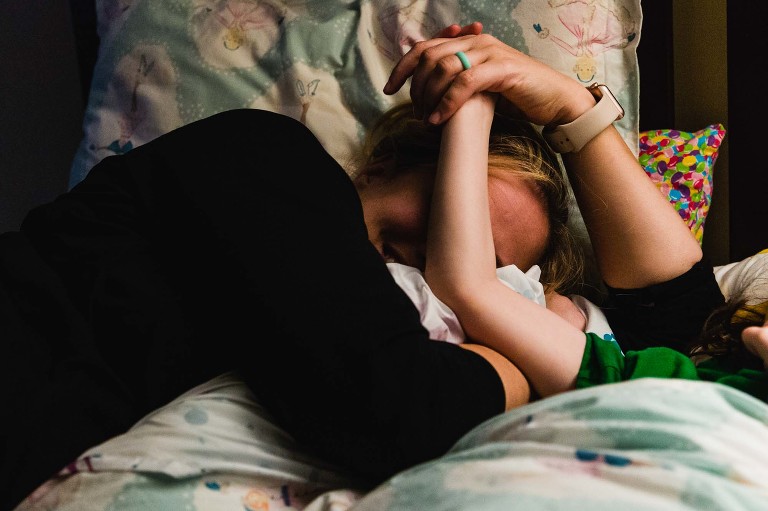 mom and daughter snuggle up at bedtime while reading, holding hands, and laughing
