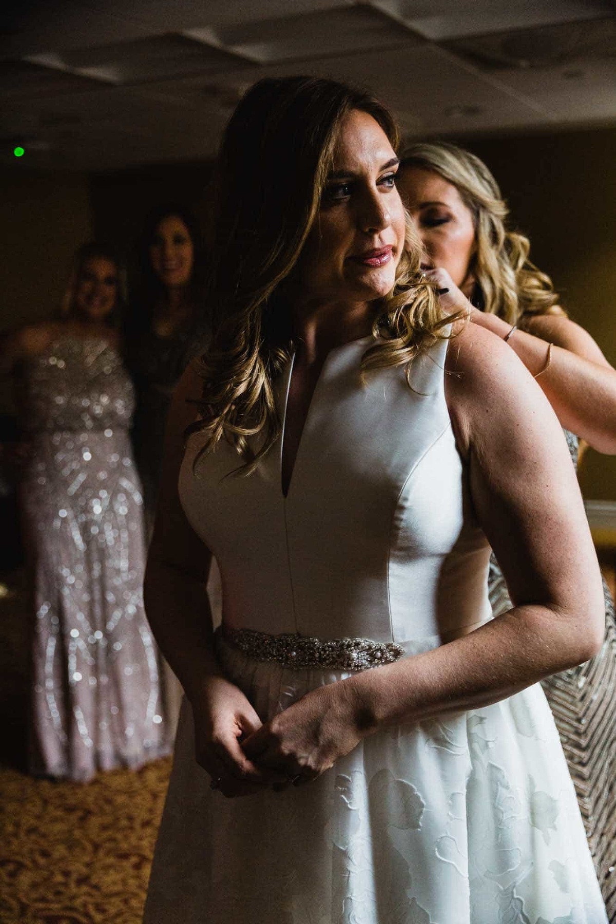 bride breathes out, while sister helps zip her into her dress. girls watch from behind. 