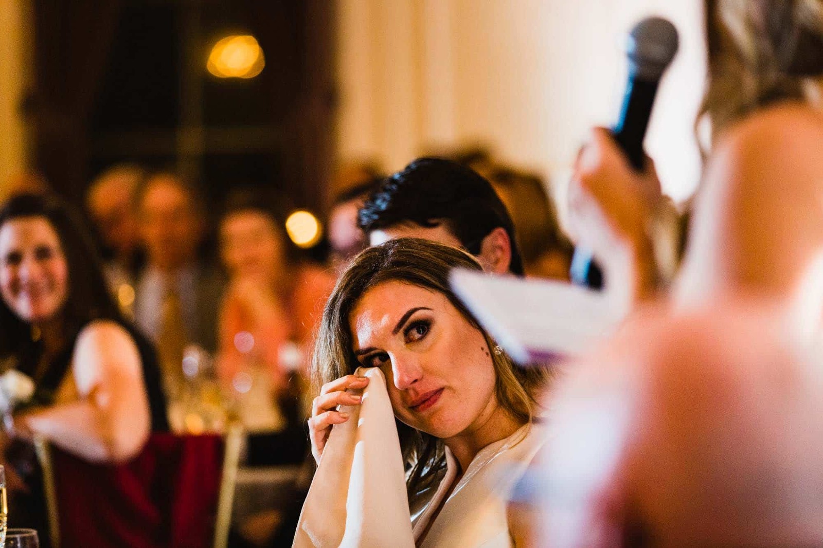 bride uses her napkin to wipe tear out of her eye, during speeches