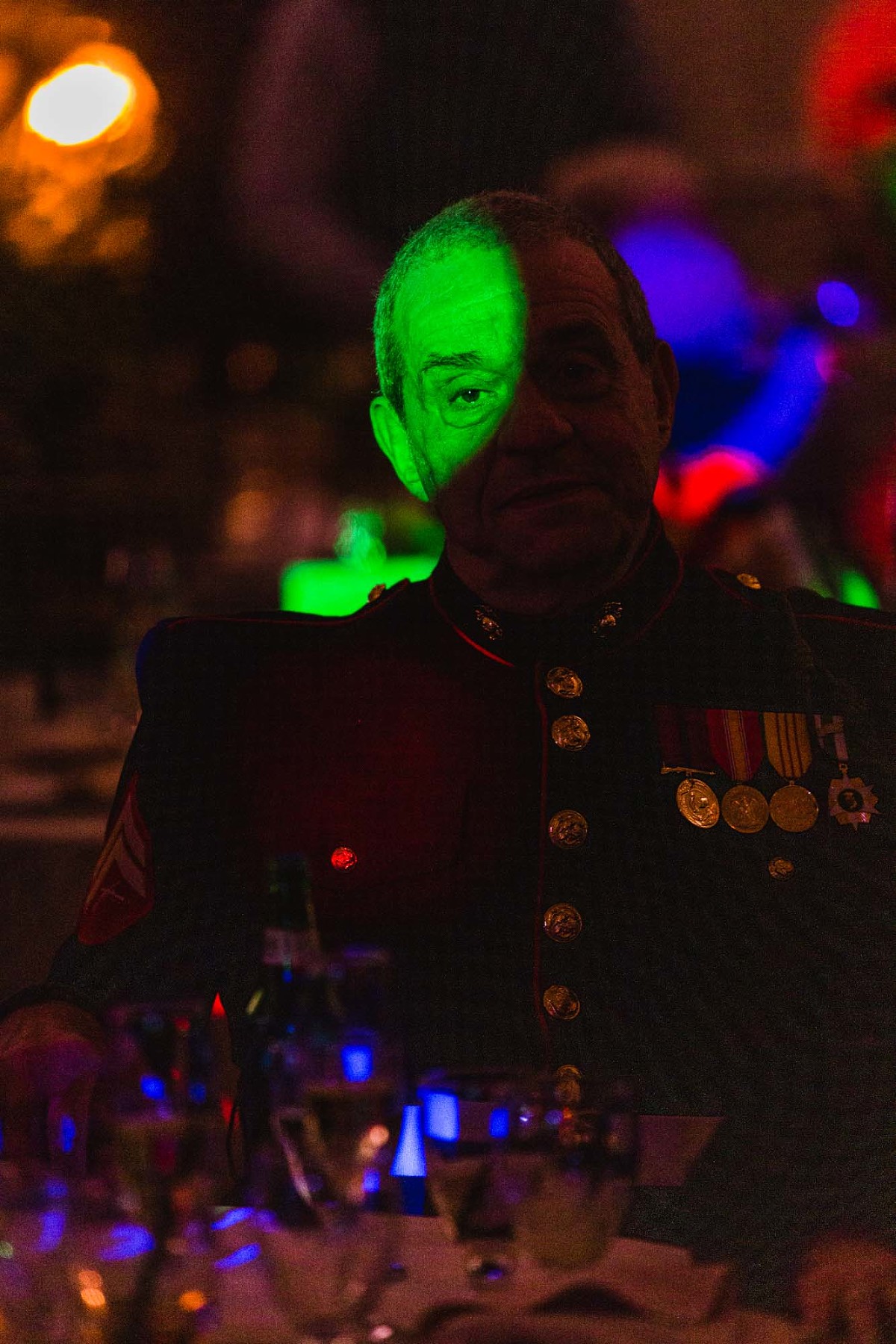 portrait of elderly man in military attire in dark room, spotlit by colorful dj lights