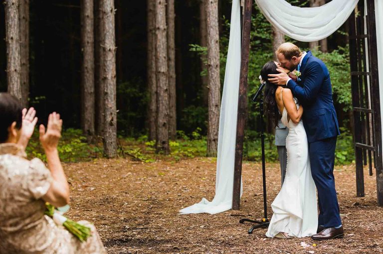 groom holds bride's face in his hands as he kisses her for the first time once they are married, with guests clapping