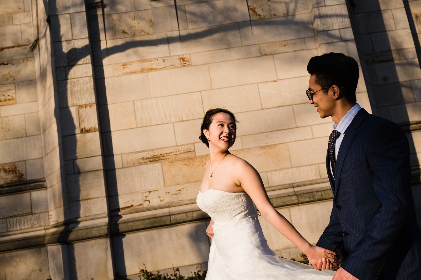 bride and groom walk together in beautiful golden light at sunset in front of the cathedral of learning. 