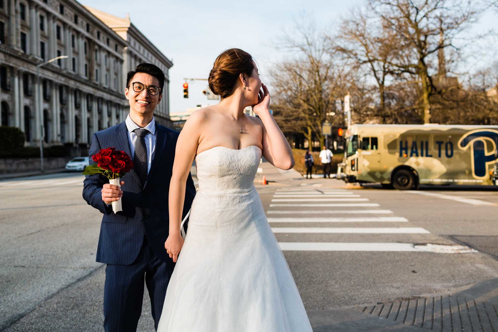 bride and groom pause on a street corner to laugh back at the scene behind them, in a casual candid moment