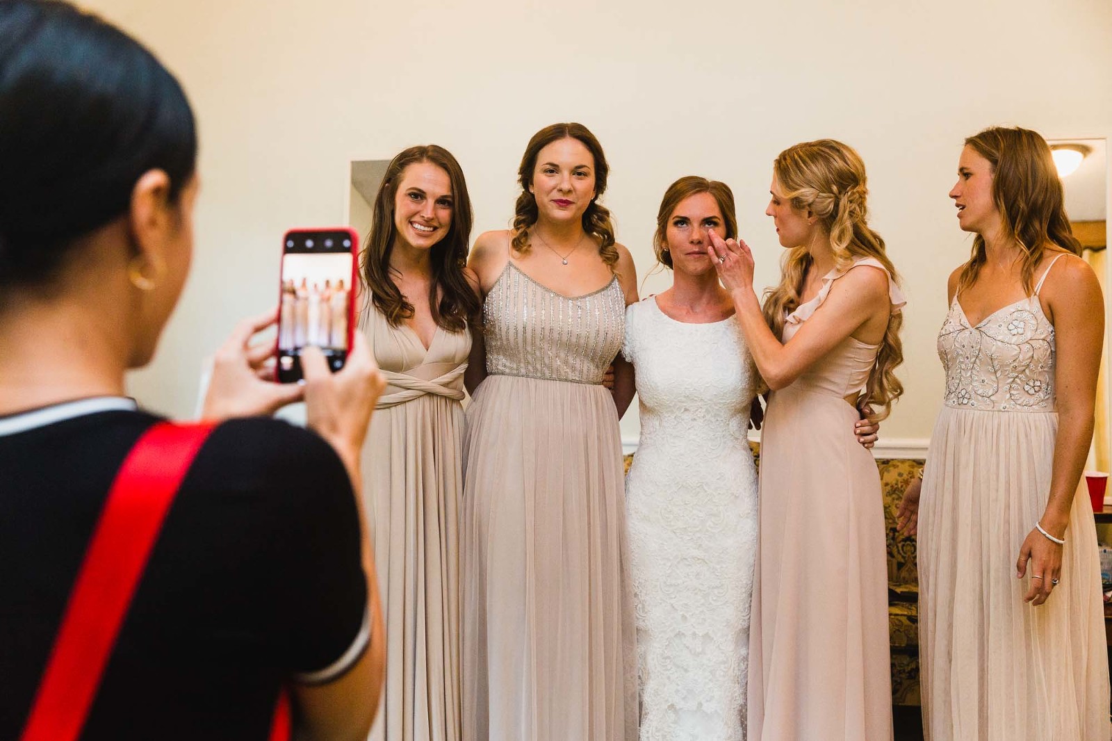 bride and bridesmaids check each other for perfection, before being photographed together. bridesmaid wipes something off bride's face. 