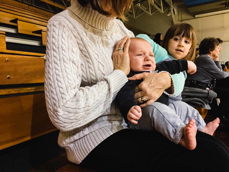 grandma holds crying baby in a loud basketball gym at st. vincent college, holding his ears