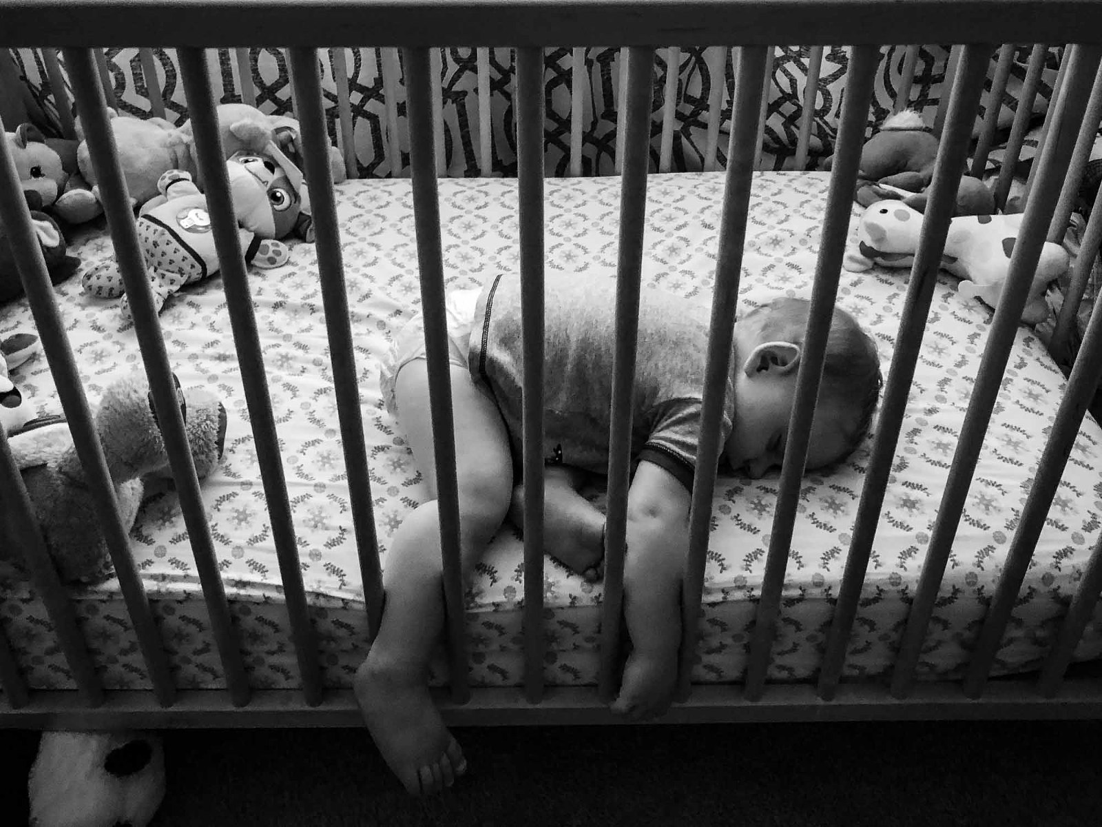 black and white grainy photo of baby asleep in crib, surrounded by toys