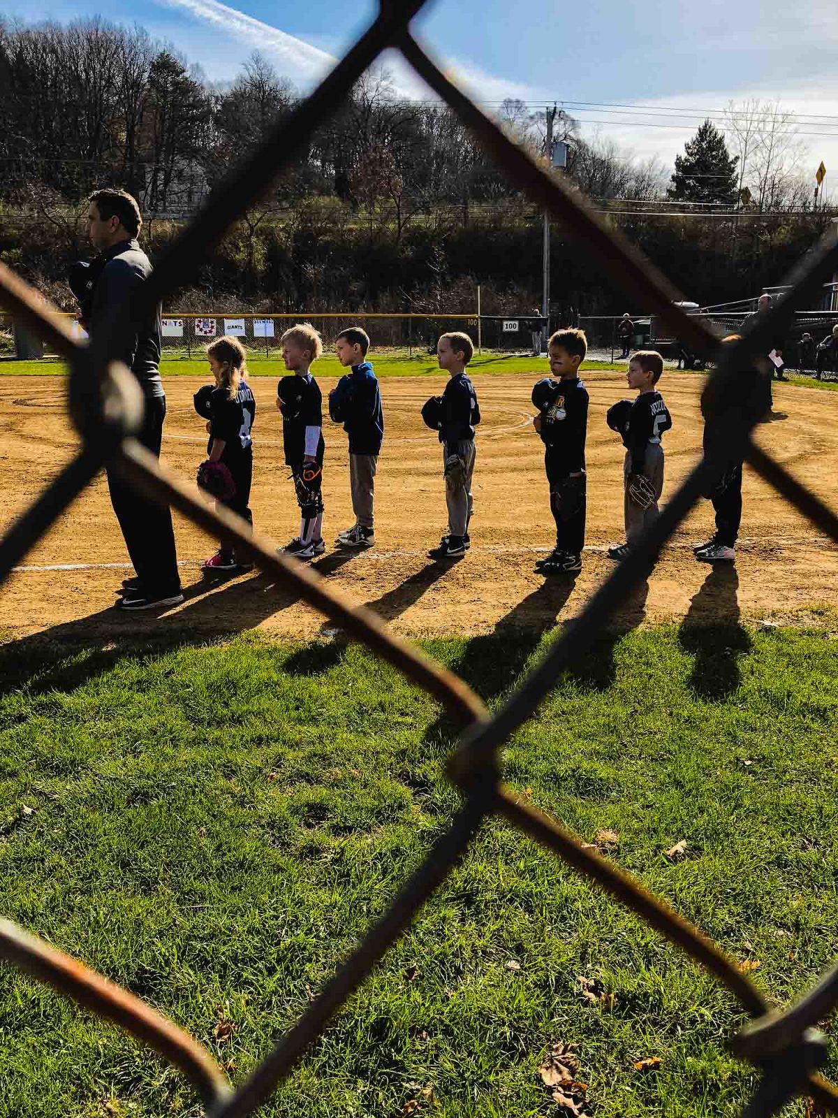 baseball team lined up for the anthem, as photographed through the chain link fence