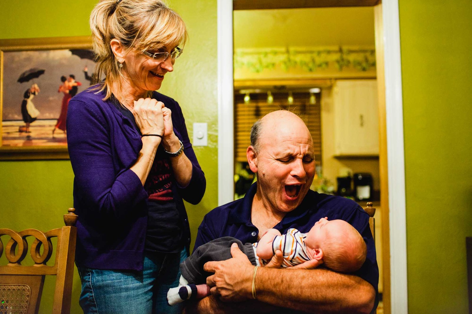 grandpa holds newborn baby and makes crazy expressions at him, while grandma also has wild expression for baby