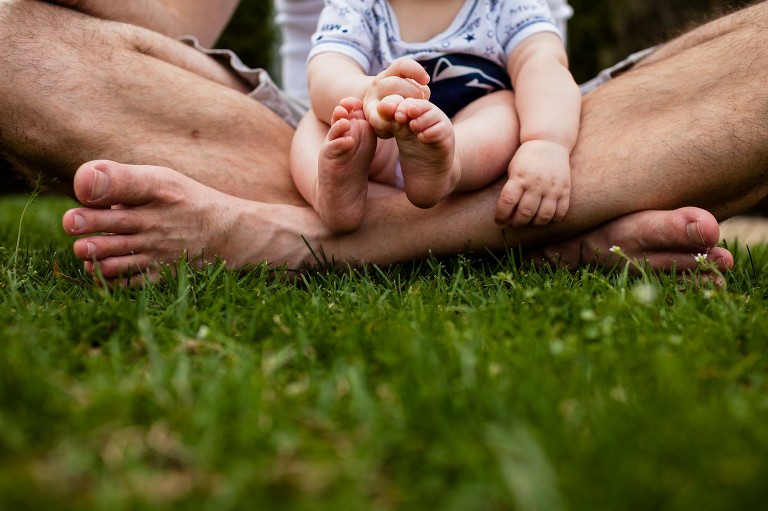 closeup of baby feet while sitting on dad's lap in the grass. lots of feet and hands!
