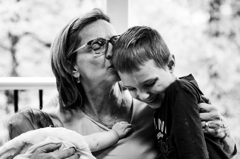 black and white photo of grandma kissing boy while holding baby, shot close up