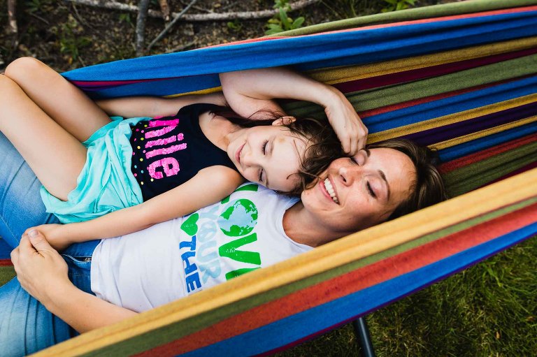 mom and daughter lying in colorful hammock together, cuddling and content