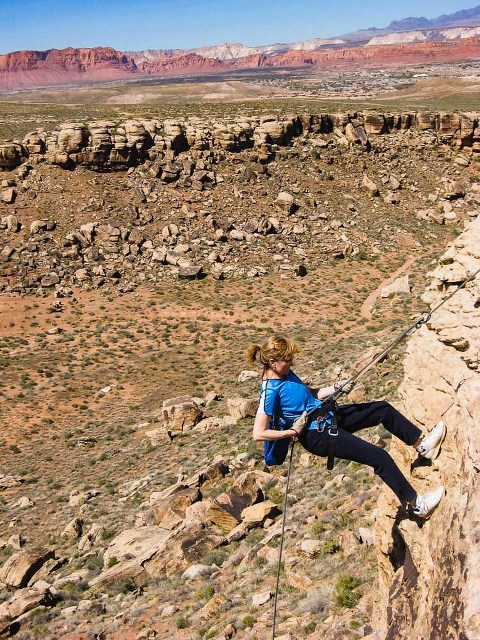 older woman dressed in blue rappelling off a cliff in utah