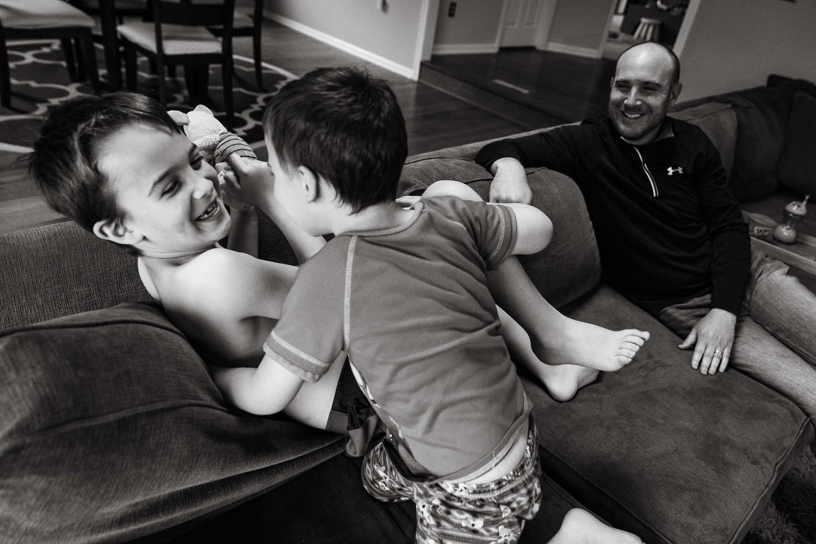 black and white photo of boys wrestling on the sofa with dad laughing in the background
