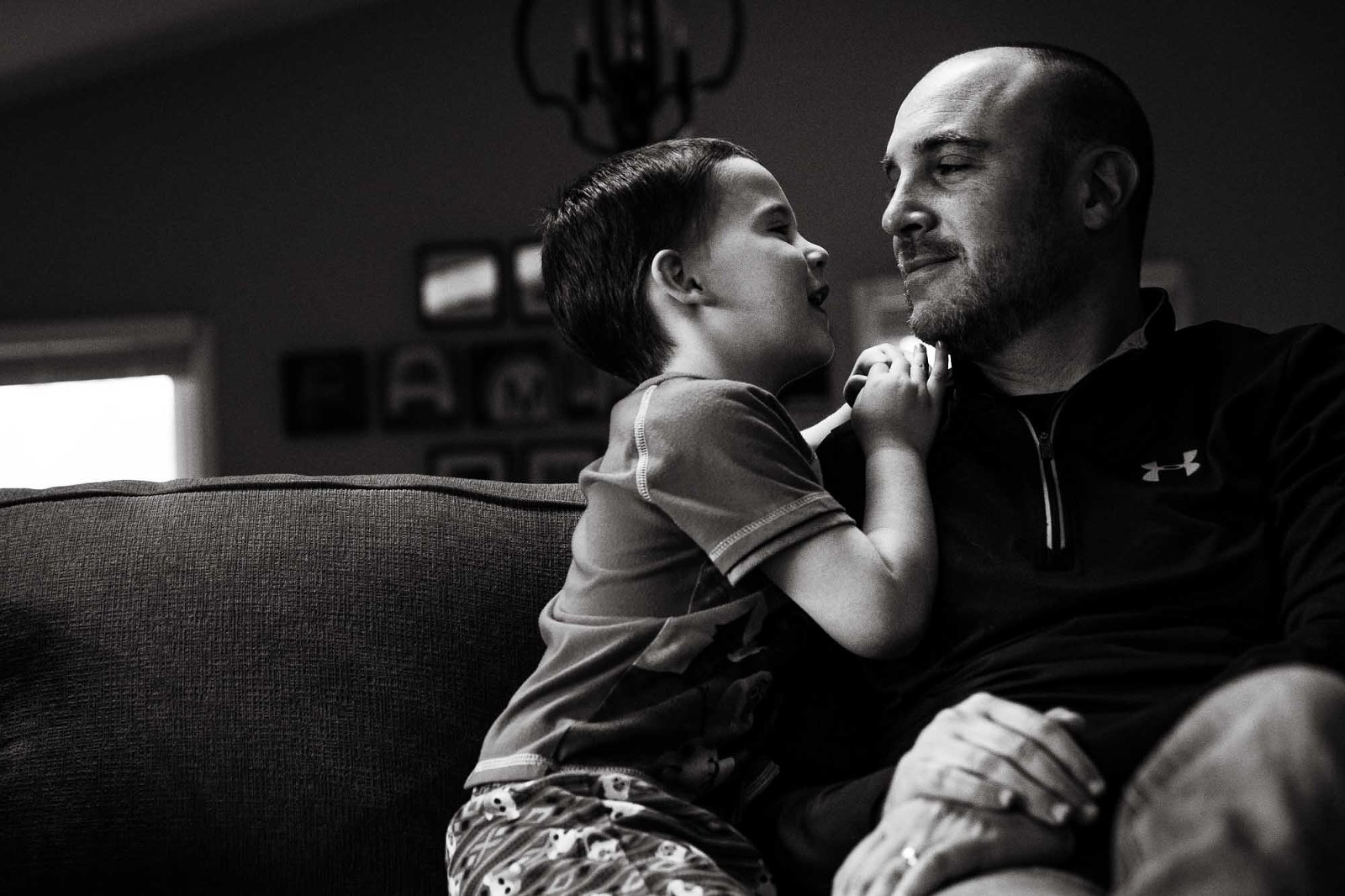 black and white photo of little boy and his dad hanging out on their couch, little boy holding onto his dad's shoulder