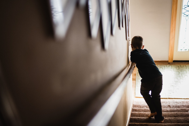 young boy running down the stairs hanging on the railing