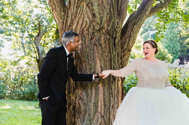 bride and groom holding hands around a tree, seeing each other for the first time on their wedding day