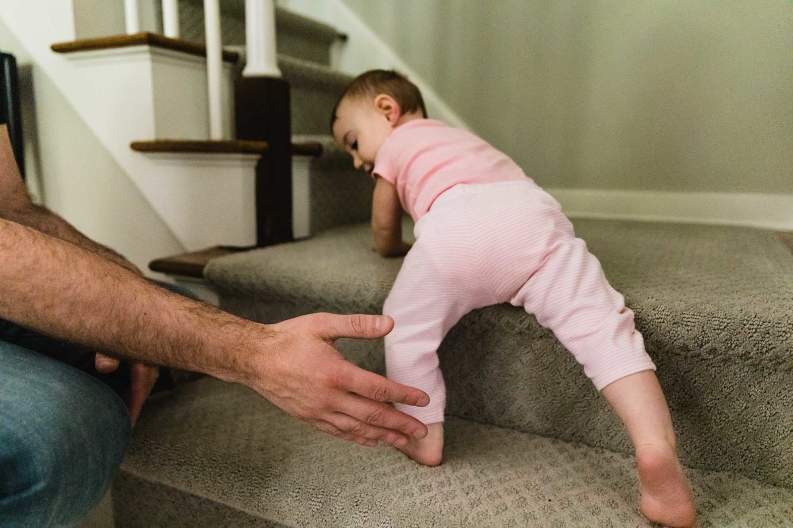 baby climbs up stairs and dad holds hand out to make sure she doesn't fall