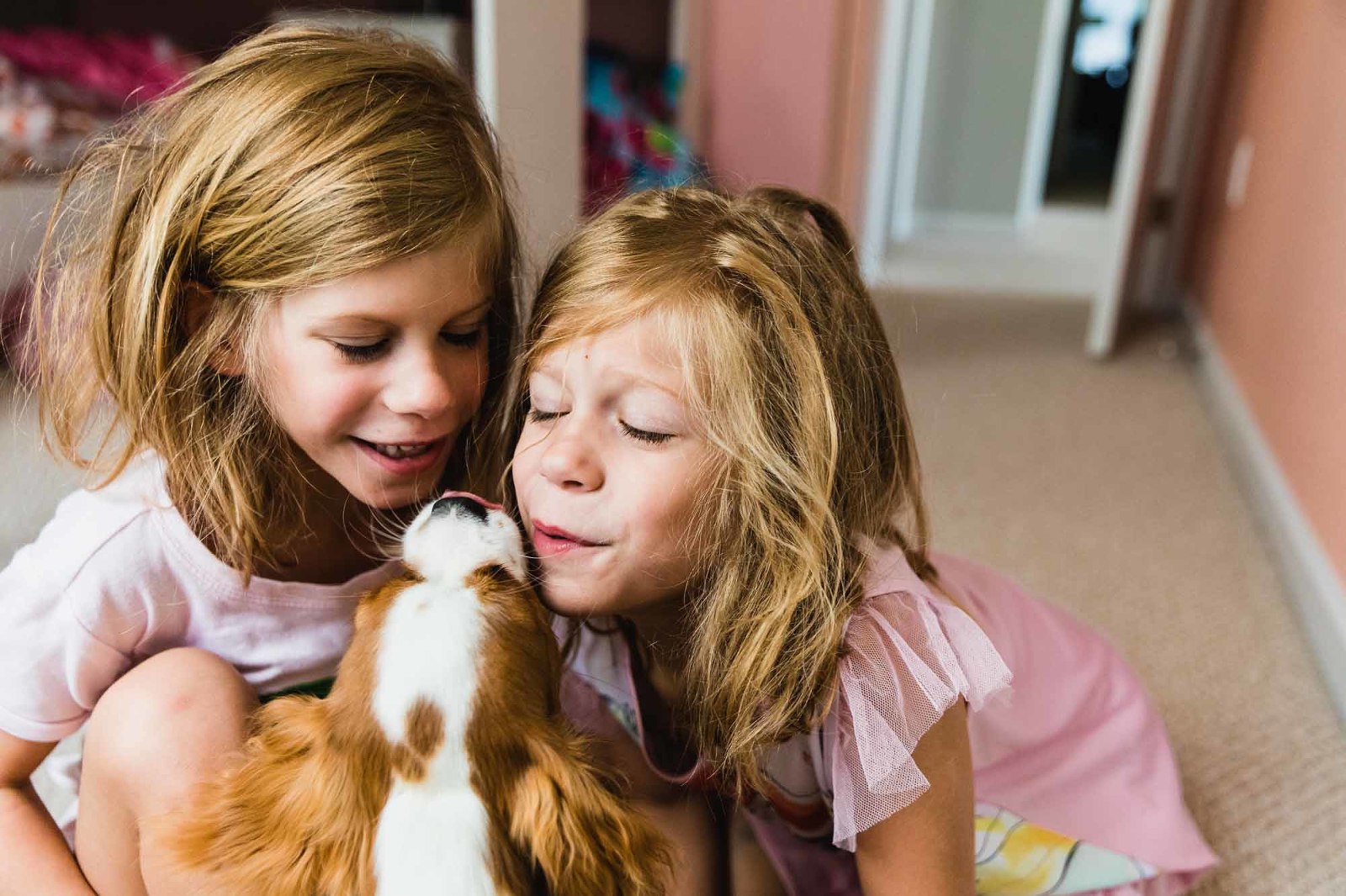 twins with bedhead and pajamas, giving kisses to their puppy on the mouth, in their bedroom. 