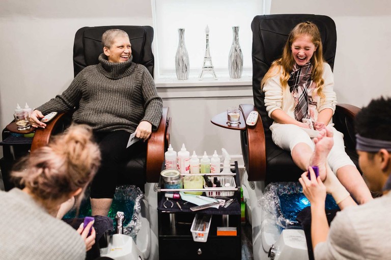 mom and daughter laughing together as they get a pedicure in a nail salon