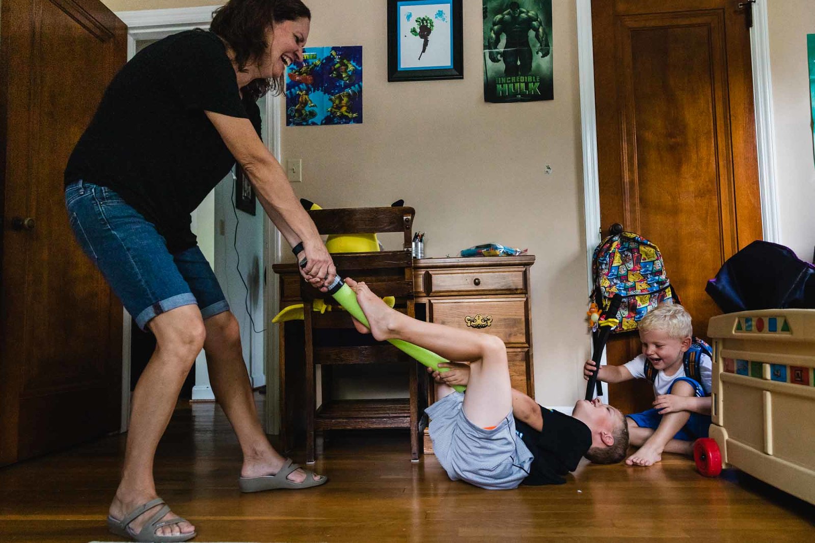 mom drags boys across the room by the feet, playing together and laughing