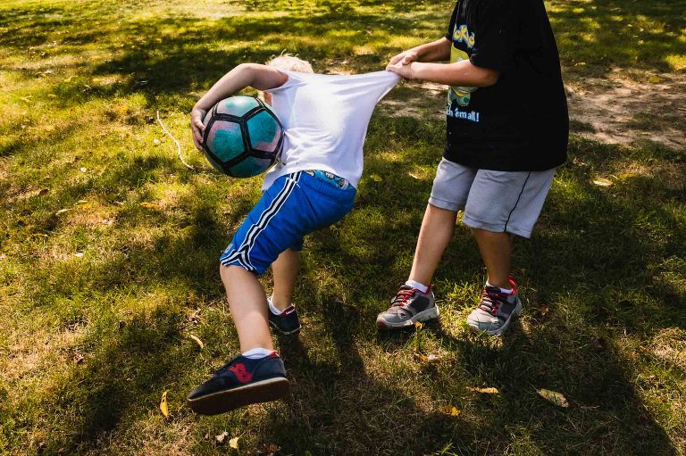 little boys play soccer with each other in their backyard, grabbing each other roughly