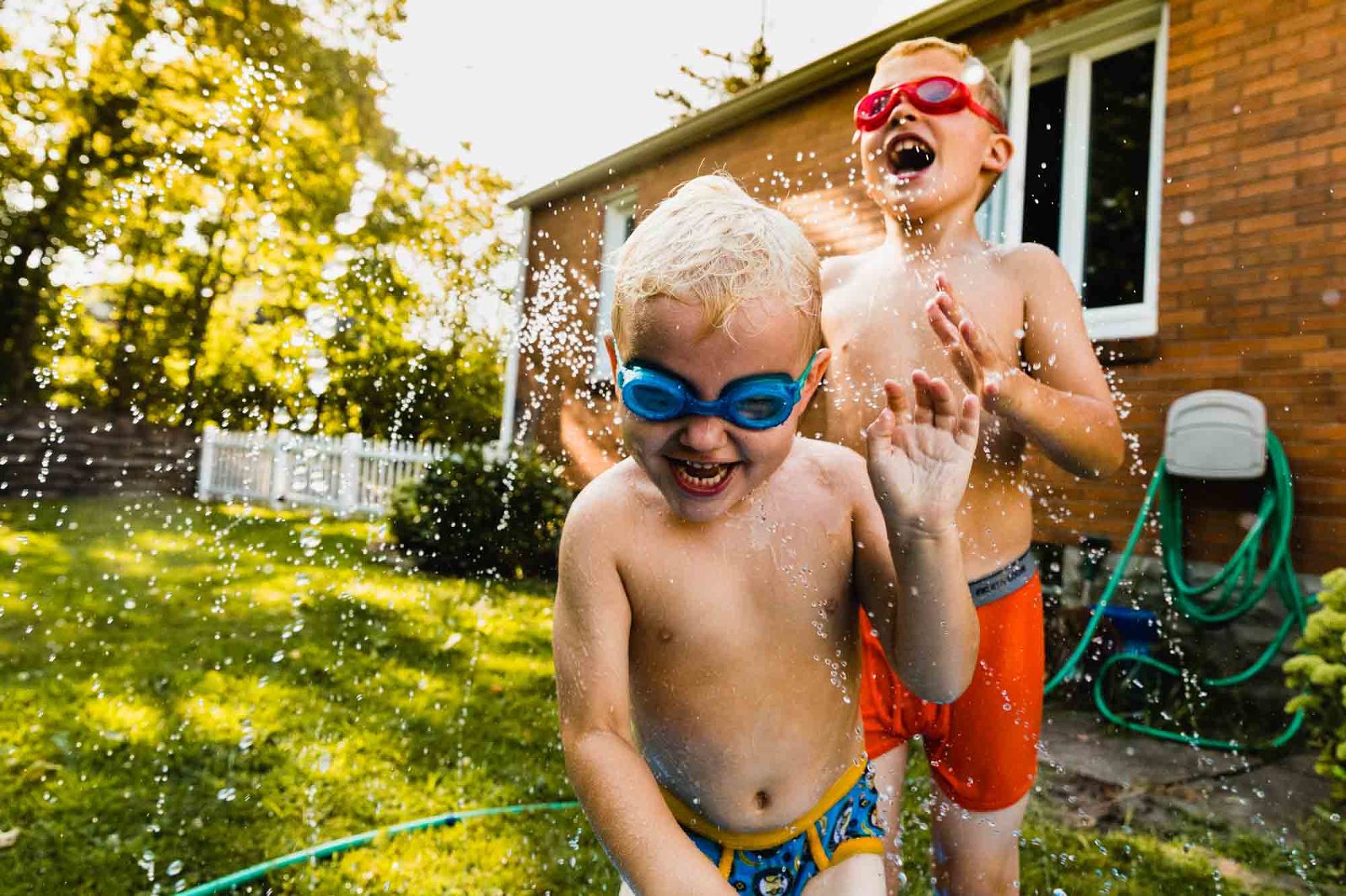two boys playing in the sprinkler in the backyard