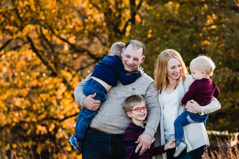 mom, dad, and their three boys snuggling together in front of warm fall foliage at sunset