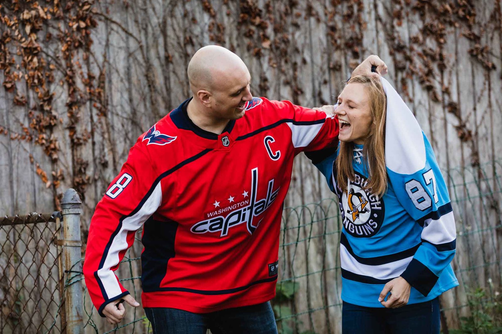 man in capitals jersey pretending to beat woman in penguins jersey, laughing