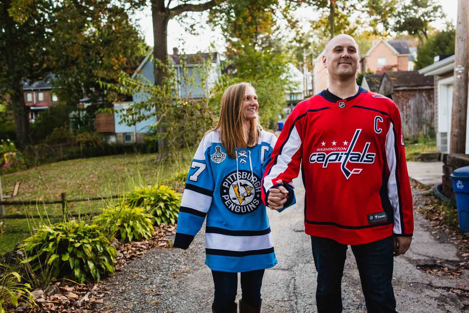 woman in penguins jersey and man in capitals jersey walking together smiling hand in hand