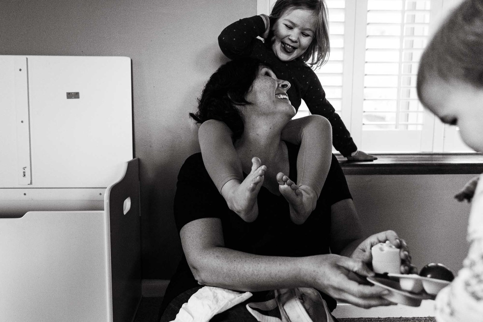 candid black and white photo of mom looking up at her daughter sitting on her shoulders, laughing together