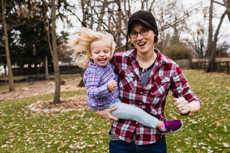 mom runs while holding toddler, hair blowing in the wind and smile across her face.