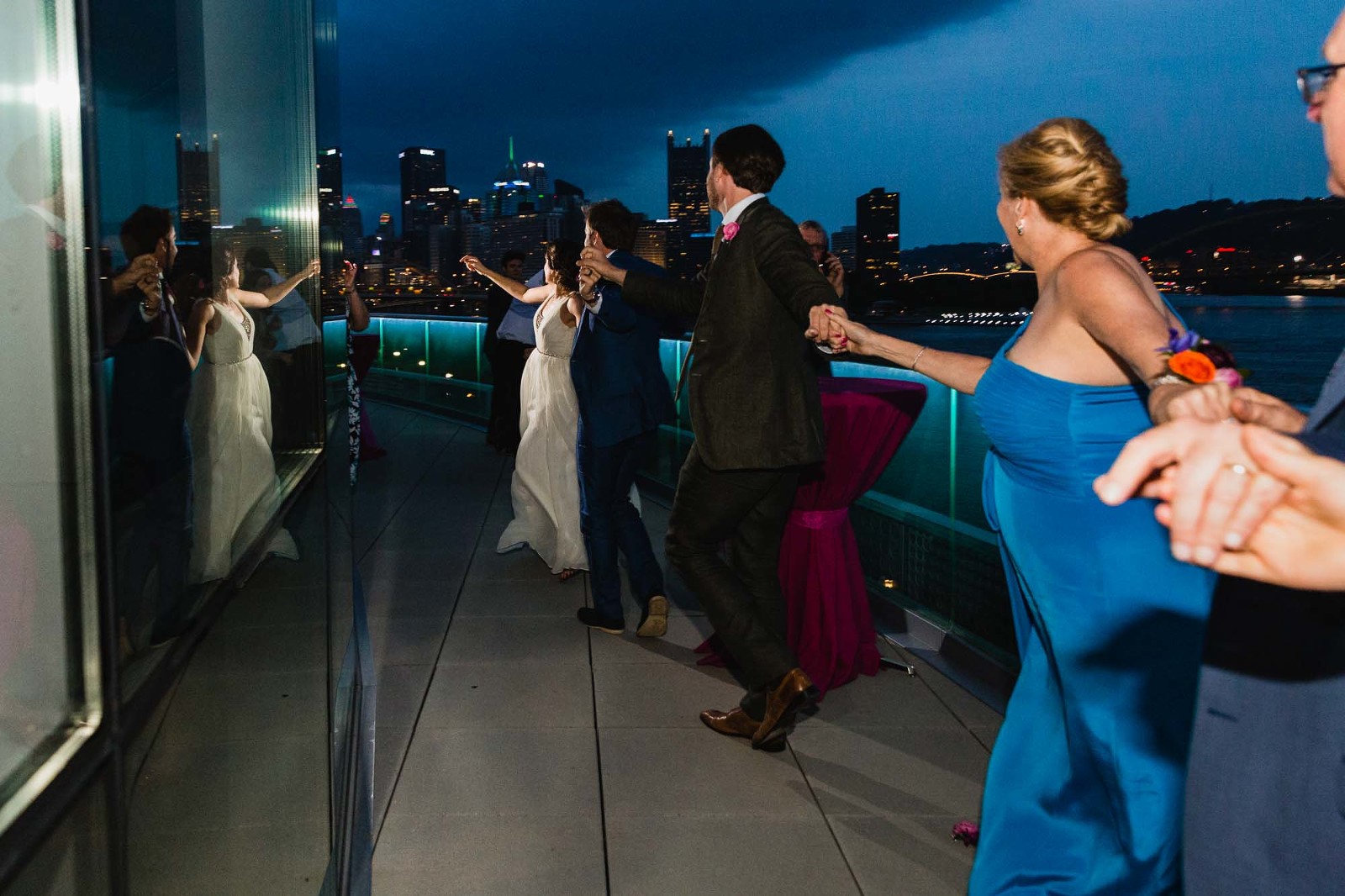 bride leads a train of wedding guests outside onto the patio at night, overlooking the city